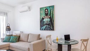A living room with a beige sofa, teal pillows, a glass coffee table, and a painting on the wall.
