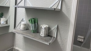 Ein Badezimmer mit weißen Wänden, einer Duschkabine und einem Ablagefach für Toilettenartikel.