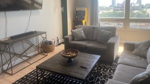 Ein Wohnzimmer mit Sofa, Couchtisch, Fernseher und einem großen Fenster mit Blick auf die Stadt.