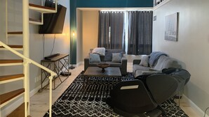 Ein modernes Wohnzimmer mit Treppe, einer Sofagarnitur, einem Couchtisch und einem großen Fenster mit Vorhängen.