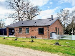 A brick house with a sloped roof, a white picket fence, and a gravel driveway.