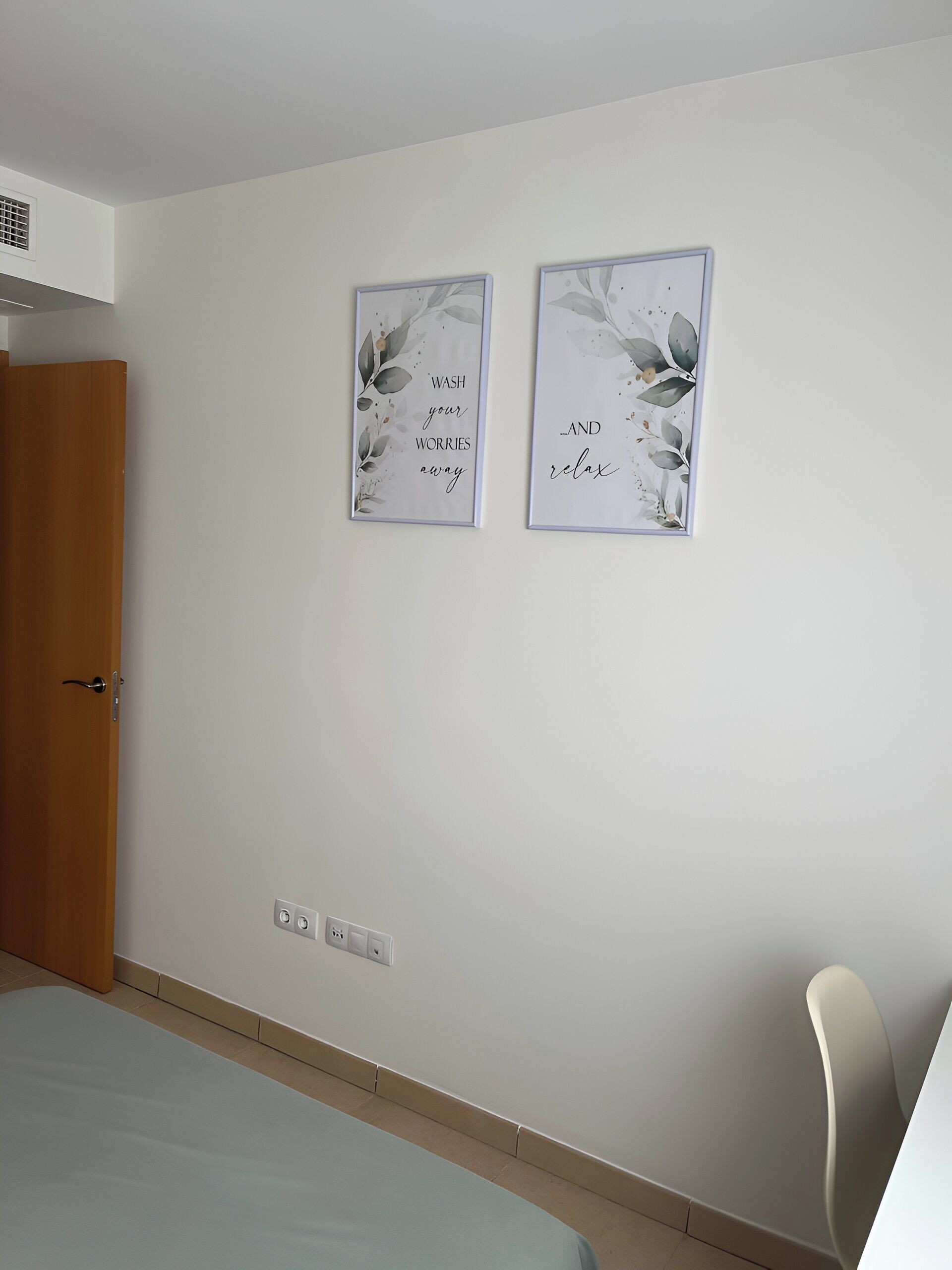 A bedroom with a bed, a door, and two wall-mounted artwork pieces with floral designs and motivational text.