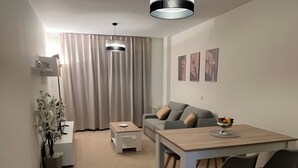Een moderne woonkamer met een bank, een eettafel met stoelen, een salontafel, een hanglamp en een potplant.