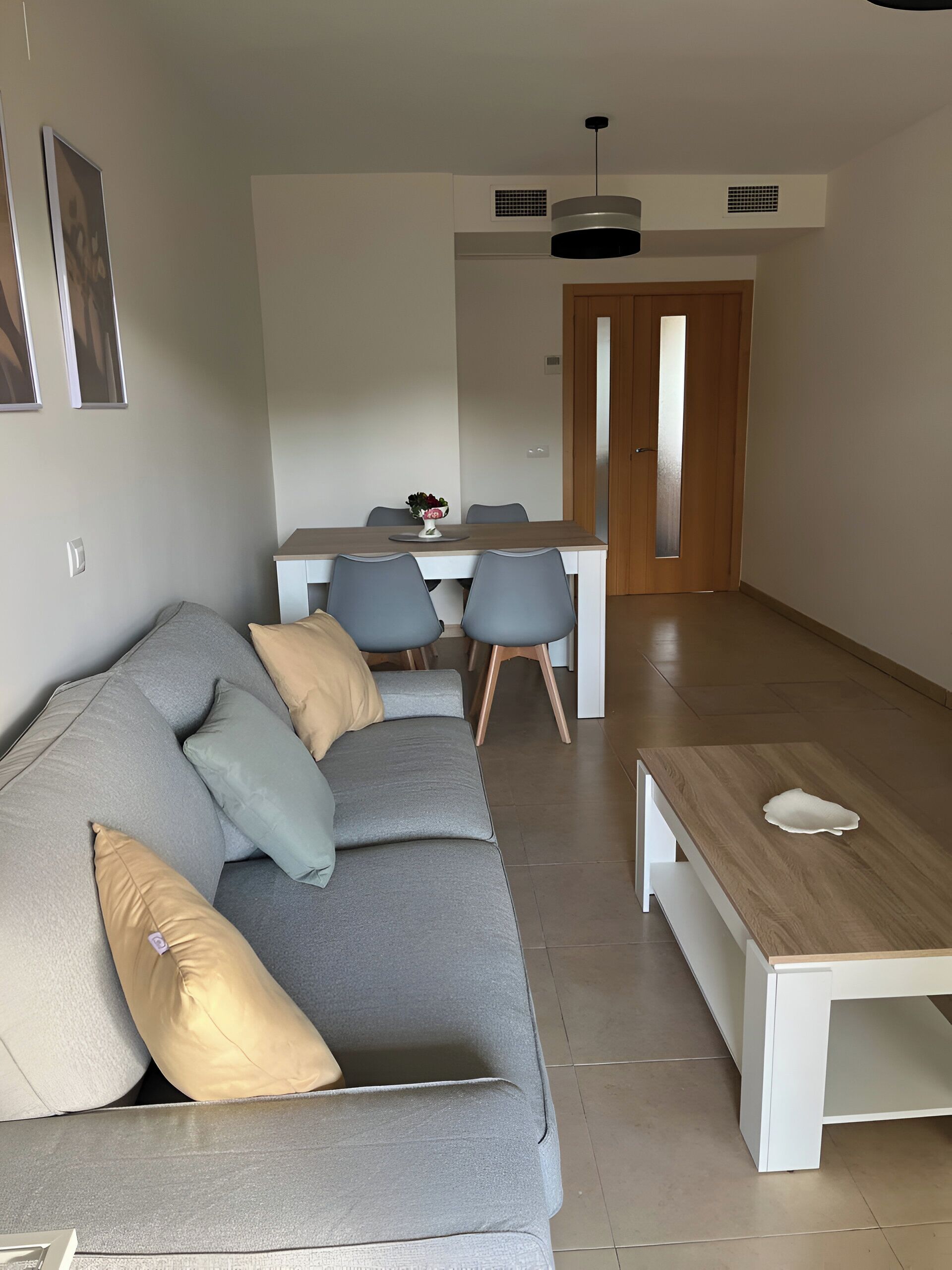 Un salon moderne avec un canapé gris, une table basse en bois et un coin repas comprenant une table blanche et des chaises grises.
