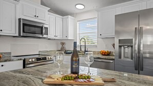 A modern kitchen with white cabinets, stainless steel appliances, a marble countertop, and a wine bottle.