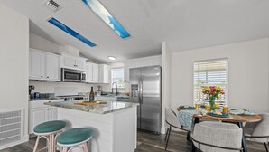 A modern kitchen with white cabinets, a stainless steel refrigerator, and a dining area with a table set for two.