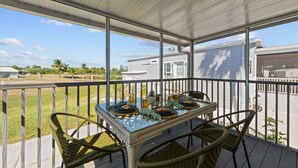 A covered outdoor patio with a table set for dining, surrounded by wicker chairs, overlooking a residential area with houses and greenery.