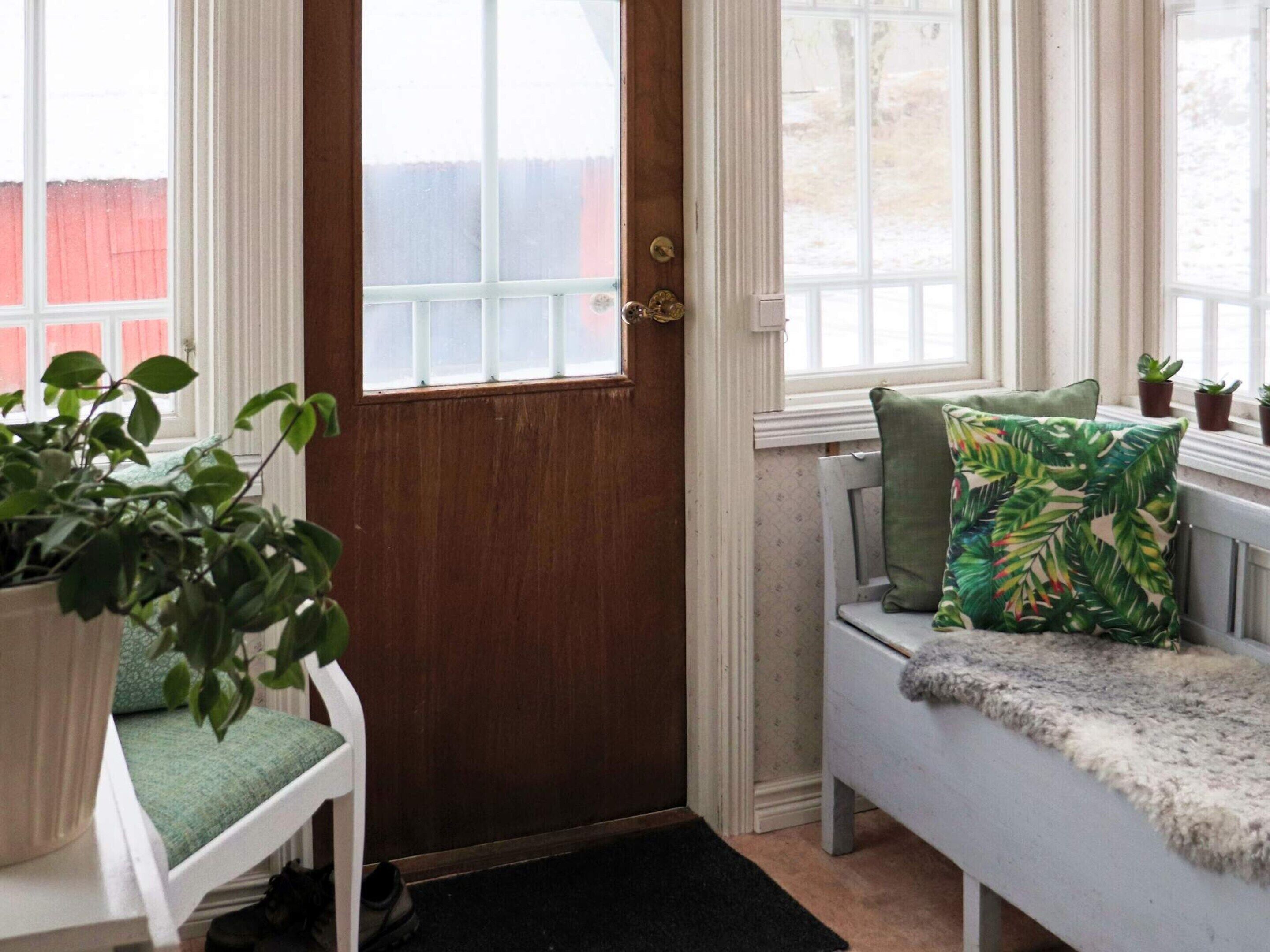 A room with a wooden door, a bench with a green pillow, and a potted plant.