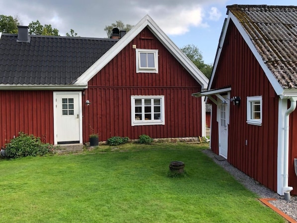 Una casa de madera roja con puerta y ventanas blancas, un pequeño jardín y una chimenea.