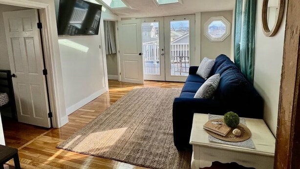 A living room with a blue sofa, a small table with decorative items, a wooden floor, and a TV mounted on the wall. - 3-bedroom beachy apartment one block from Hampton Beach (Hampton)