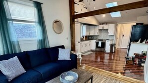 A modern living room with a dark blue sofa, a wooden coffee table, and a large window with curtains. - 3-bedroom beachy apartment one block from Hampton Beach (Hampton)
