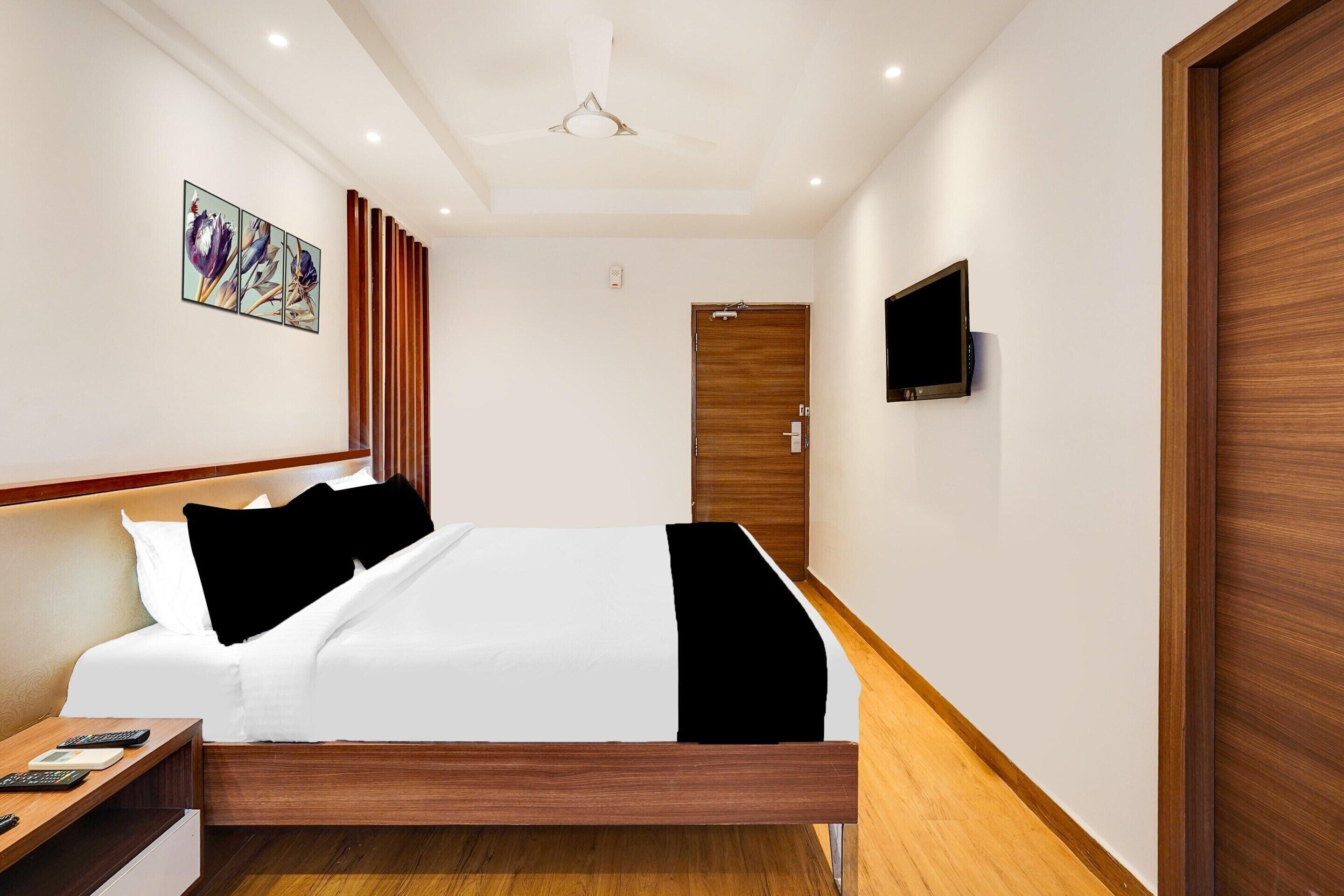 A modern hotel room with a wooden bed frame, a flat-screen TV mounted on the wall, and a ceiling fan.