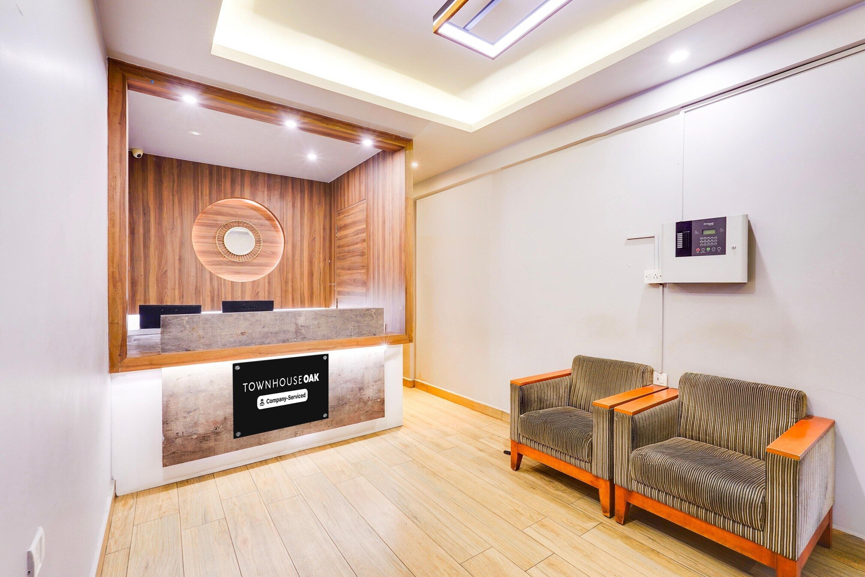 Zona de recepción con mostrador de madera, área de estar con sillas a rayas y panel de control en la pared.