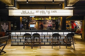 Uma área de bar com um letreiro neon, banquetas e diversas garrafas.