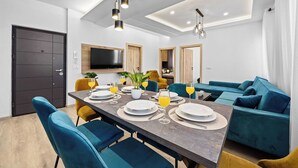 A modern dining area with a long table set for four, blue chairs, and a TV mounted on the wall. - 2 Bedroom Charming Apartment in Pula (Pula)