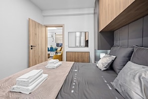 A modern hotel room with a bed, a wooden door, a small desk, a chair, and a mirror on the wall. - 2 Bedroom Charming Apartment in Pula (Pula)