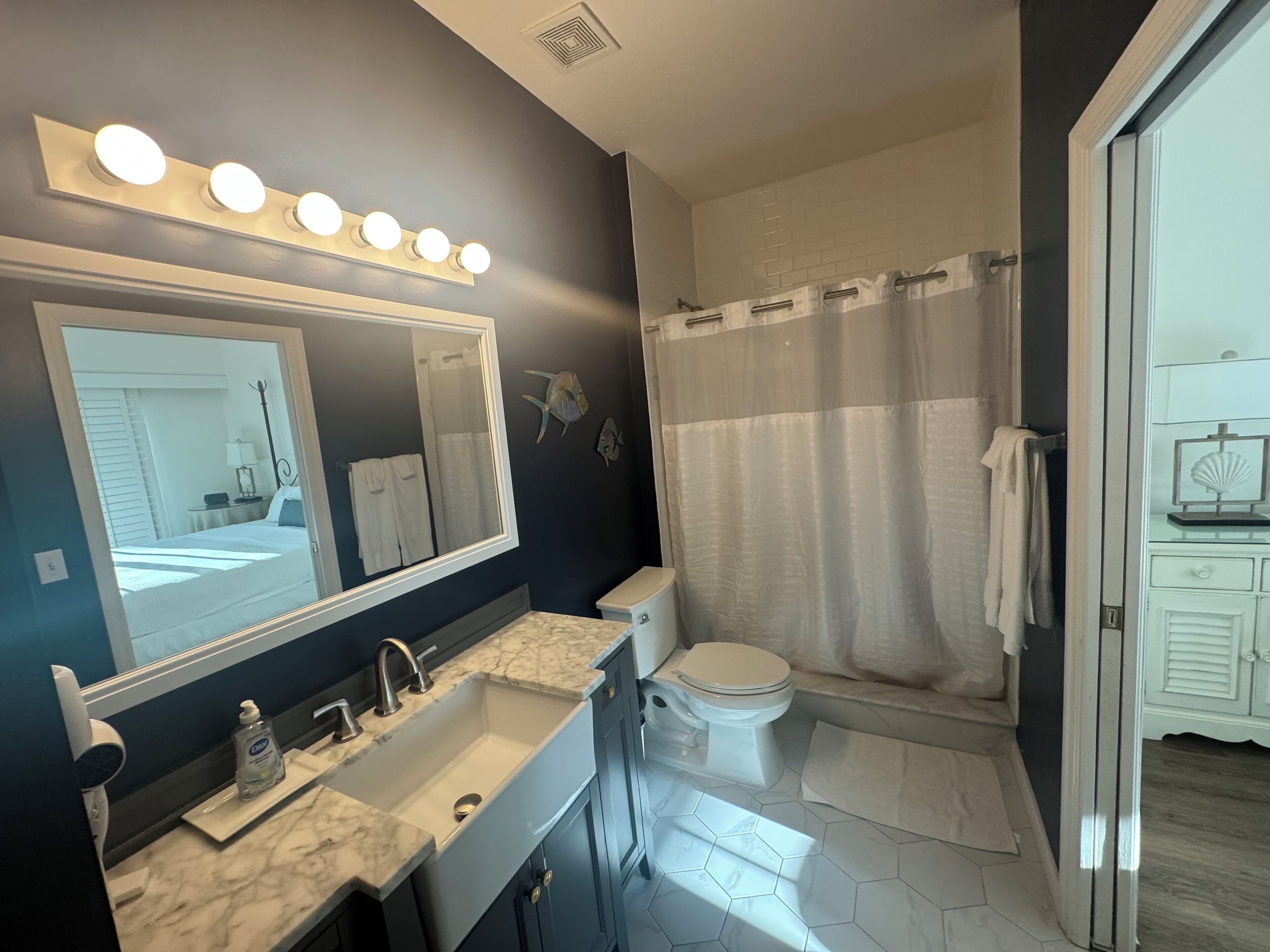 A bathroom with a large mirror, two sinks, a toilet, and a shower with a curtain.