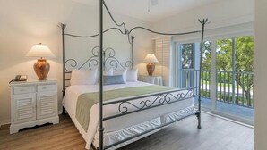 Een bed met baldakijn, met een metalen frame, witte beddengoed en twee bedlampjes.