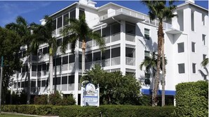 Een meerhoog hotel met balkons, palmbomen en een bord dat een restaurant en winkelruimtes aangeeft.