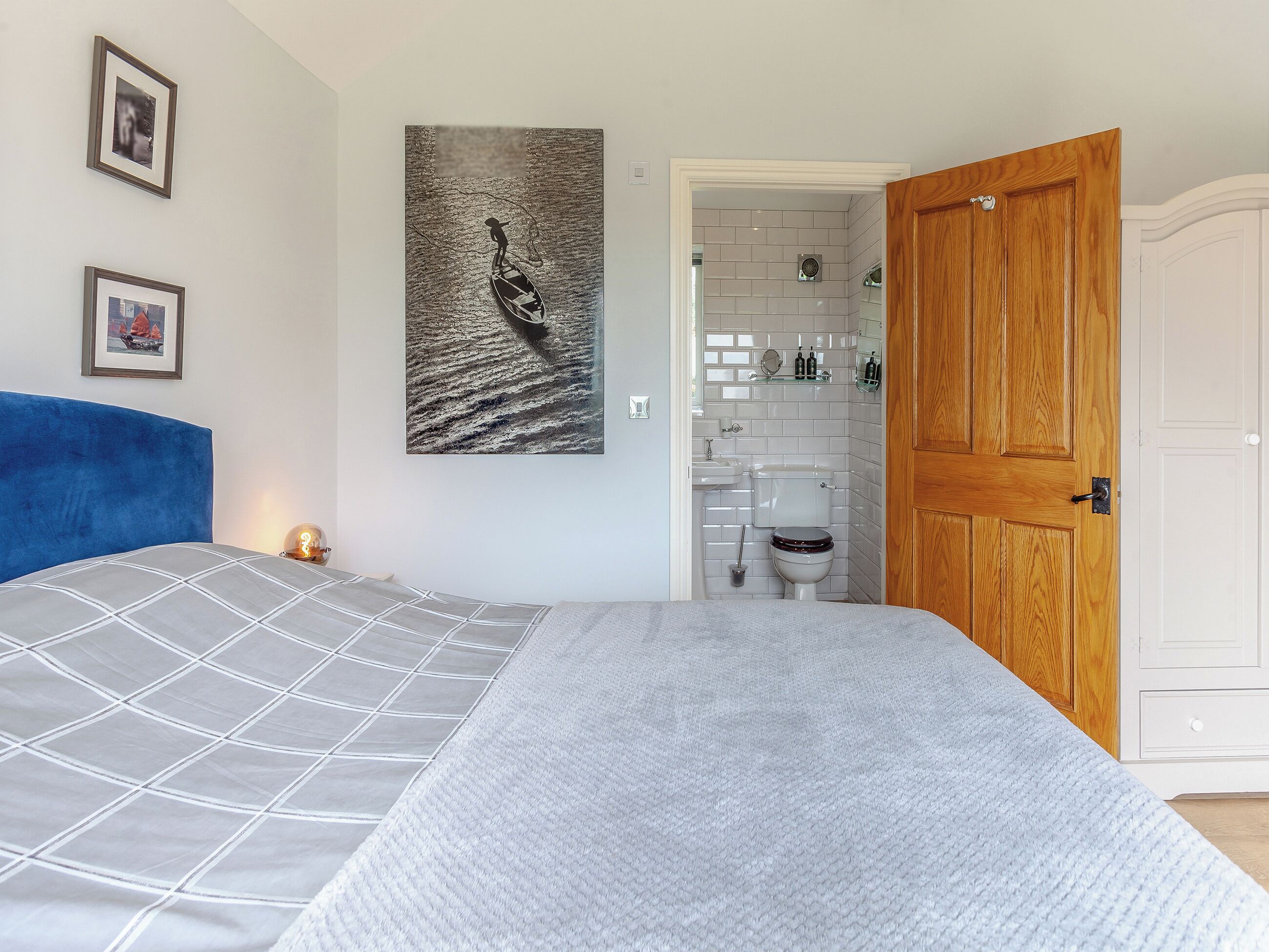 A bedroom with a bed, a wall-mounted picture, a wooden door, and a bathroom visible through an open door.