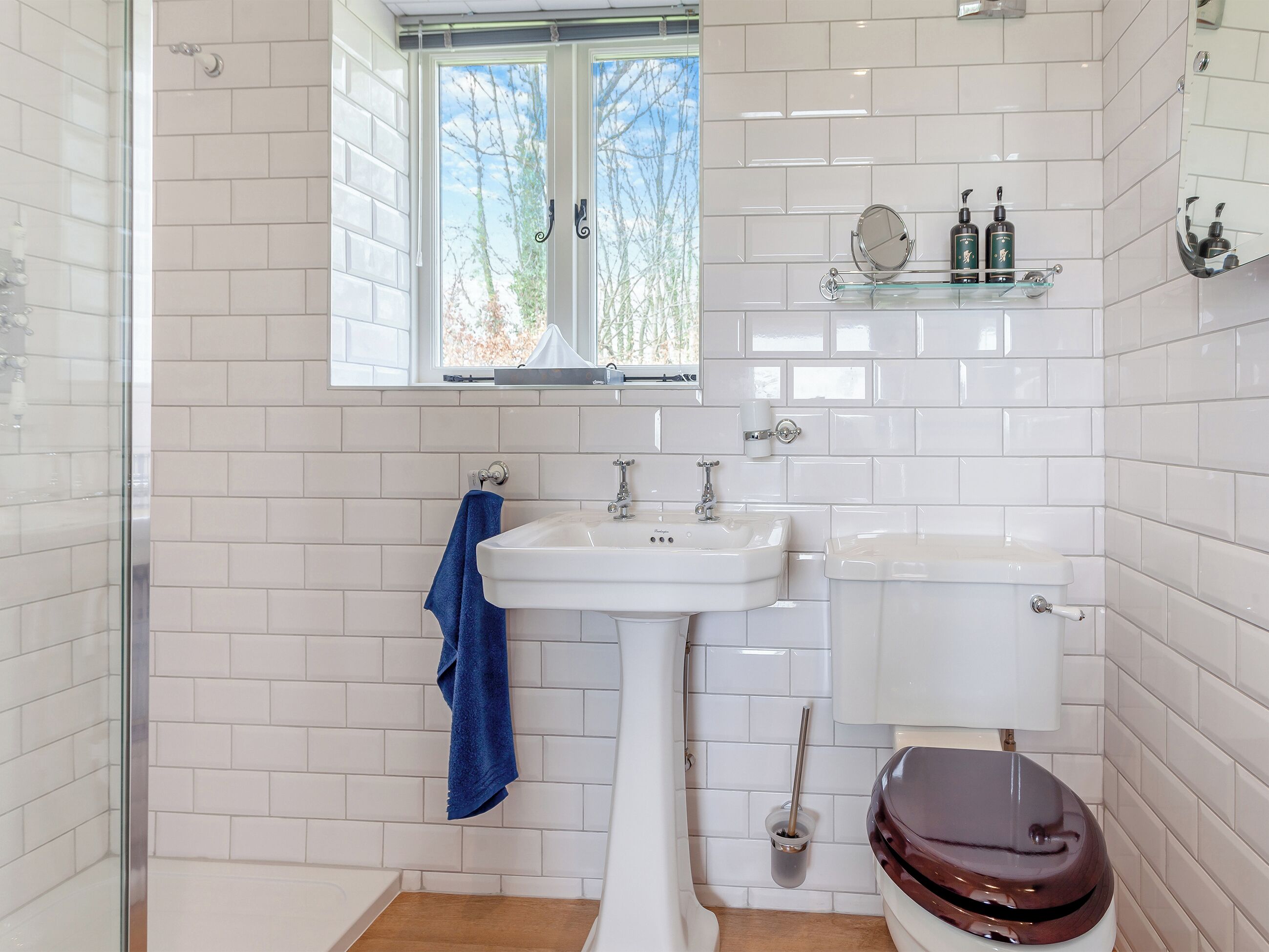 Ein Badezimmer mit weißen Fliesen, einem Waschbecken, einer Toilette, einem Fenster und einem blauen Handtuch.