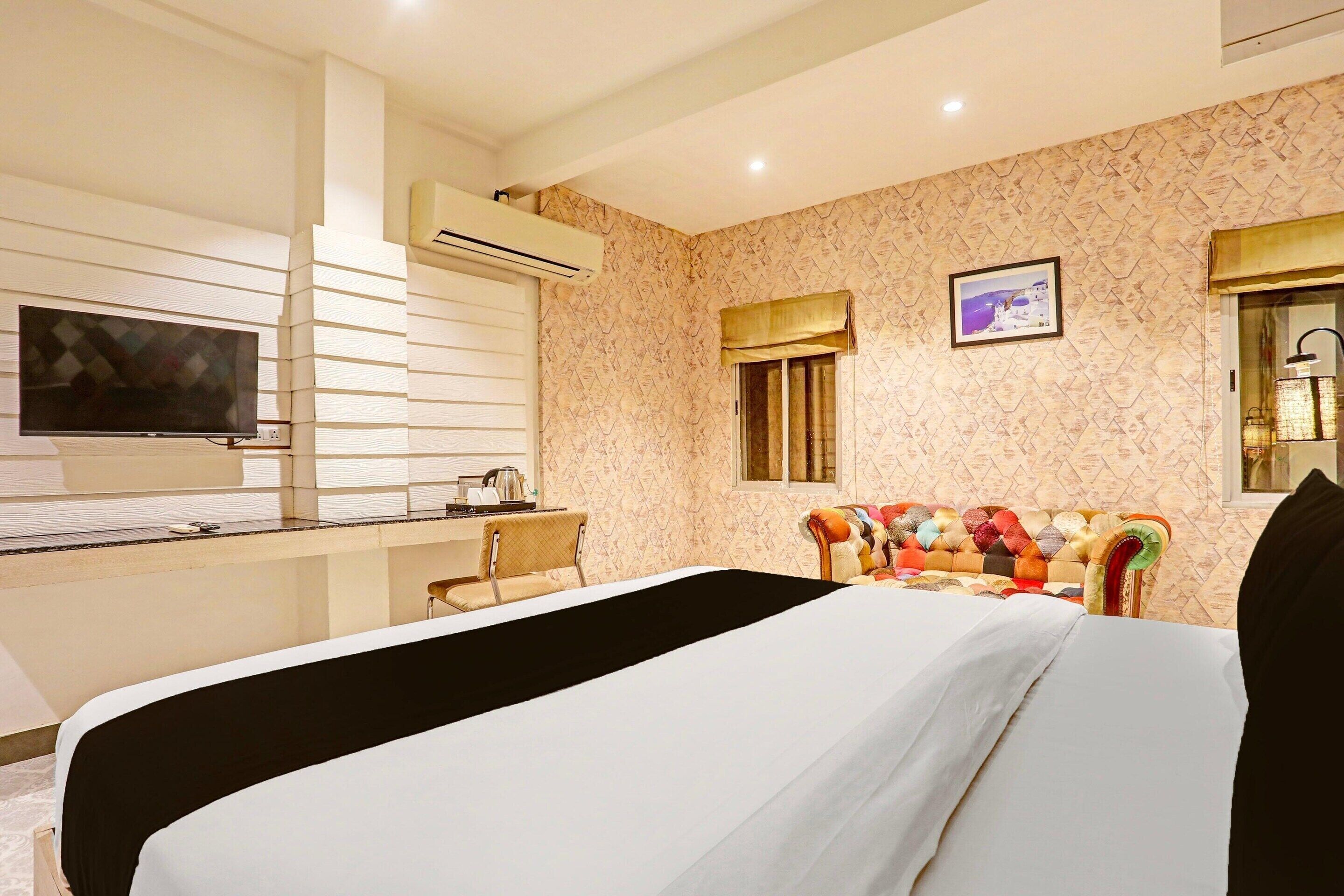 A hotel room with a bed, a TV, a window with curtains, a sofa, and a wall-mounted air conditioner.