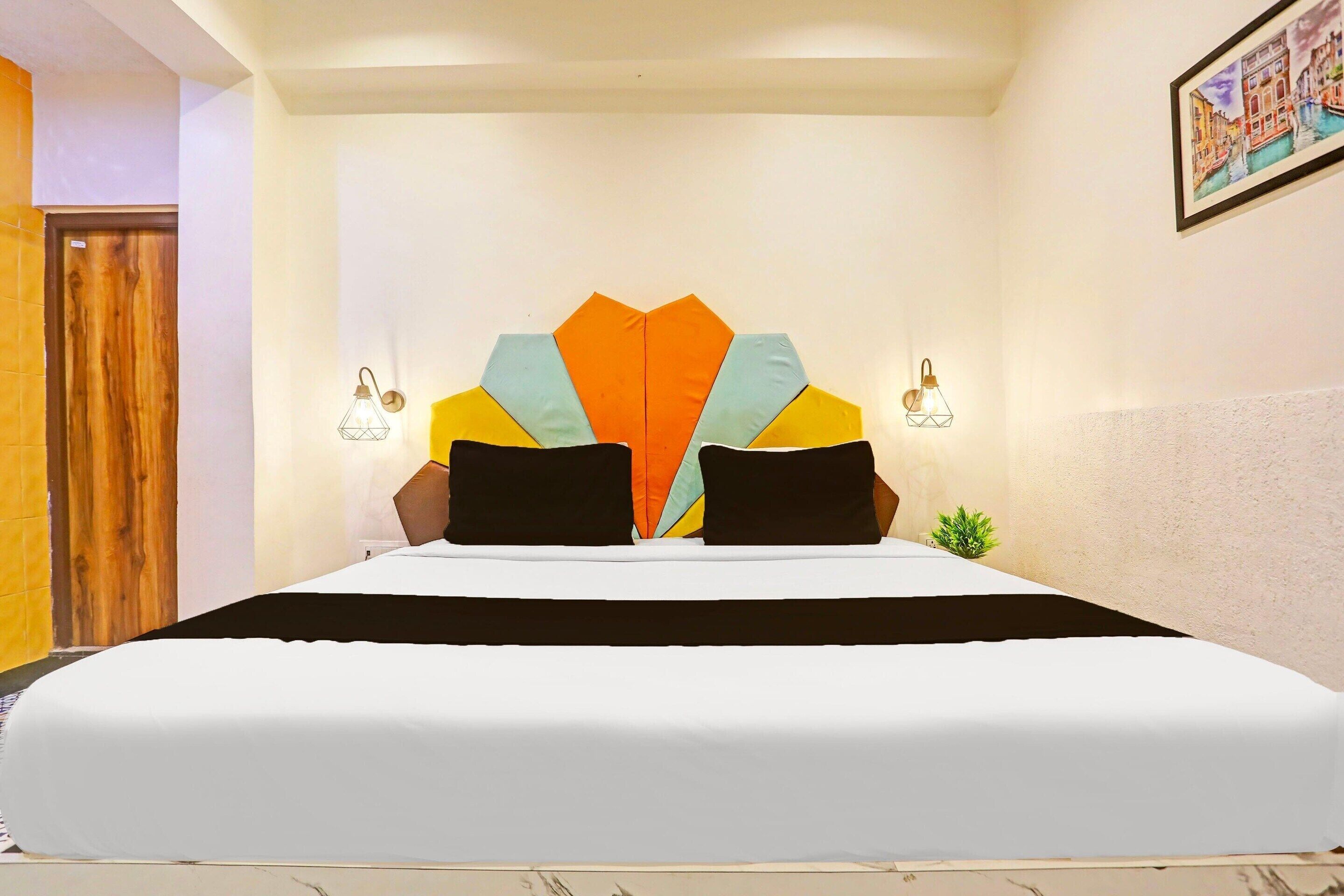 Een hotelkamer met een groot bed, een decoratieve hoofdbord, twee wandlampen en een kleine plant.