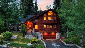 A two-story log cabin with a stone foundation, a garage, and a well-maintained front yard with a stone pathway.