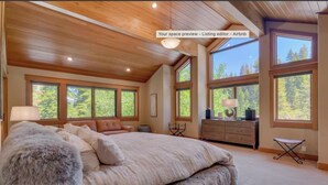 A spacious bedroom with a large bed, multiple windows, and a wooden ceiling.