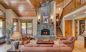 A spacious living room with a stone fireplace, leather sofas, and a staircase leading to an upper level.