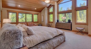 A spacious bedroom with a large bed, multiple windows, and a wooden ceiling.