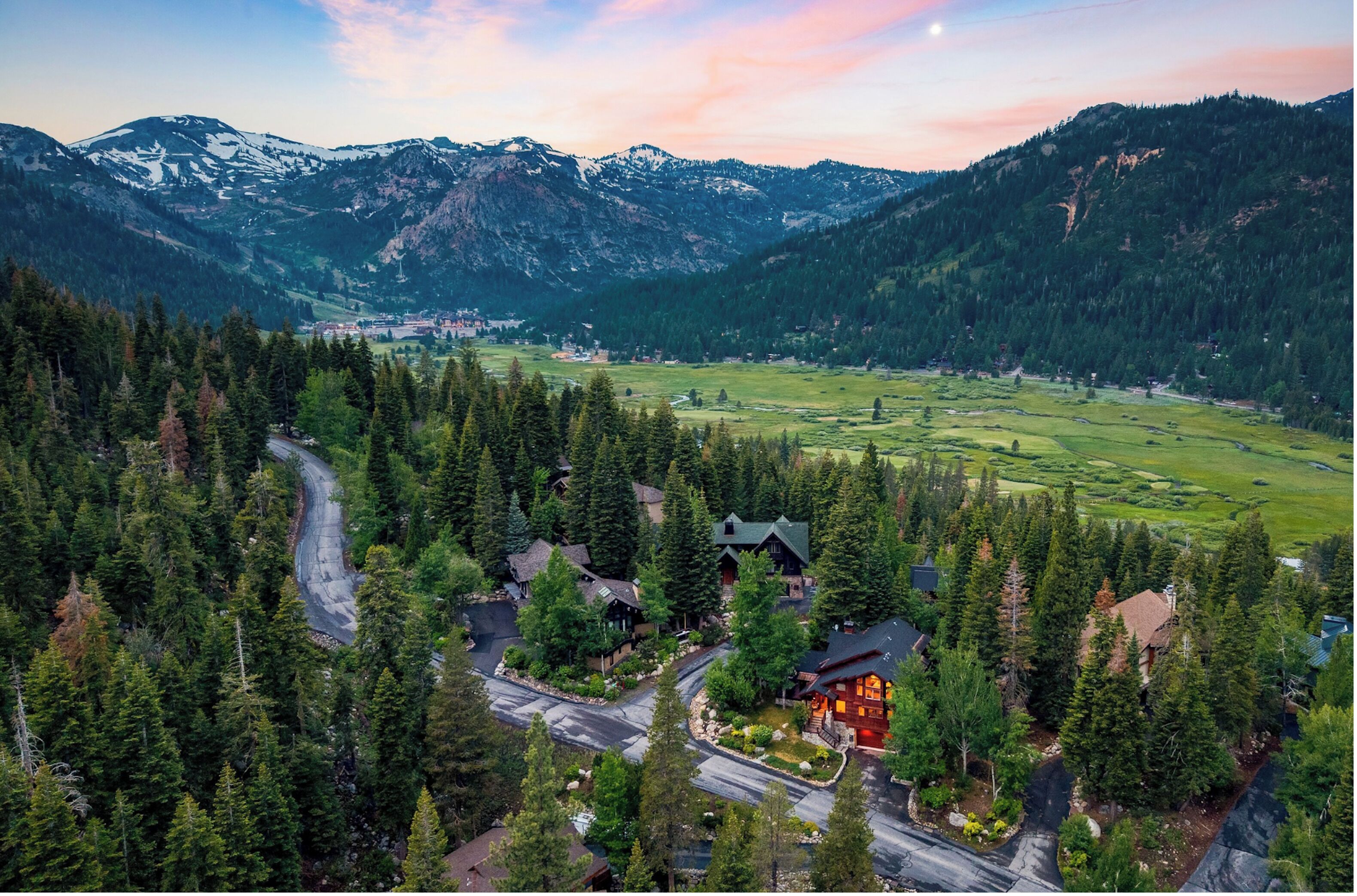 A mountainous landscape with a lodge surrounded by dense forest and a winding road.