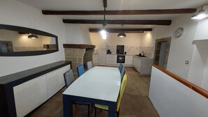 A compact kitchen with a dining area, featuring a white table, blue chairs, and a stone fireplace. - Quiet 3-star gite for 6 to 8 people with view, 5min from St Guilhem le désert (Arboras)