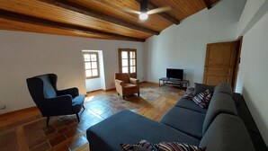 A spacious living room with a wooden ceiling, a grey sofa, a black armchair, and a small television on a wooden stand. - Quiet 3-star gite for 6 to 8 people with view, 5min from St Guilhem le désert (Arboras)