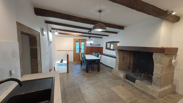 A kitchen with a stone fireplace, a dining area with a table and chairs, and a hallway leading to another room. - Quiet 3-star gite for 6 to 8 people with view, 5min from St Guilhem le désert (Arboras)