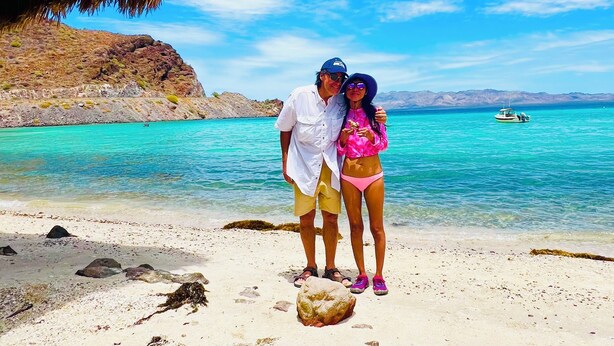 A couple standing on a beach with clear turquoise water and a boat in the distance. - Brand new Loft in Loreto! Short walk to the beach, marina, and downtown! (Loreto)