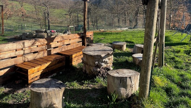 A wooden pergola with string lights, a wooden bench, and a rustic seating area with a view of a grassy field and trees in the background. - Home for nature lovers, 5 minutes from the village (Valleto)
