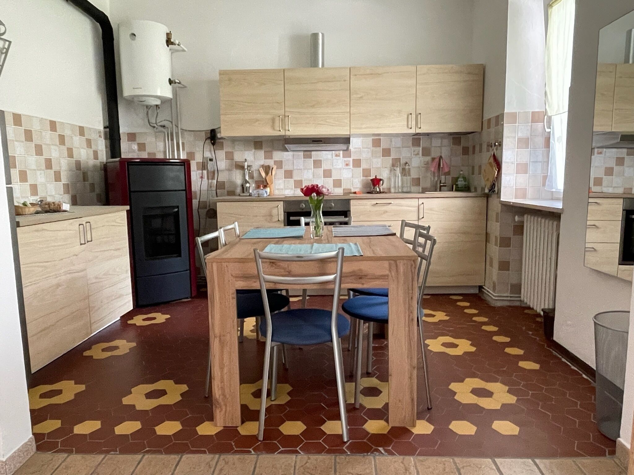 Une cuisine avec des meubles de rangement en bois, une table à manger avec des chaises, un four rouge et un pare-feu en carreaux.