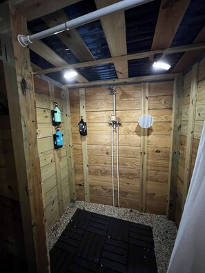 A wooden shower stall with a black rubber mat, wooden walls, and a ceiling with exposed beams.