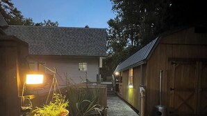 A narrow pathway leading to a house with a sloped roof, surrounded by wooden structures and potted plants.