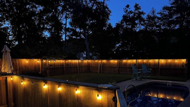 A backyard with a wooden deck, string lights, a pool, and a chair.