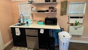 A compact kitchen with a sink, a microwave, a refrigerator, and a small window with blinds.