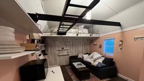 A compact living space with a loft bed, a sofa, a coffee table, and a kitchen area with a microwave.