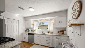 Een moderne keuken met witte kastjes, een granieten aanrecht, een vaatwasser en een raam met uitzicht op de omgeving.