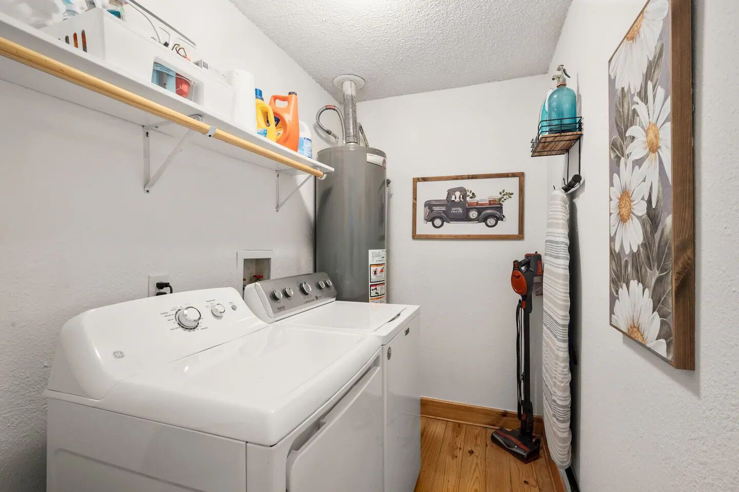 A laundry room with a front-loading washer and dryer, a water heater, and a vacuum cleaner.