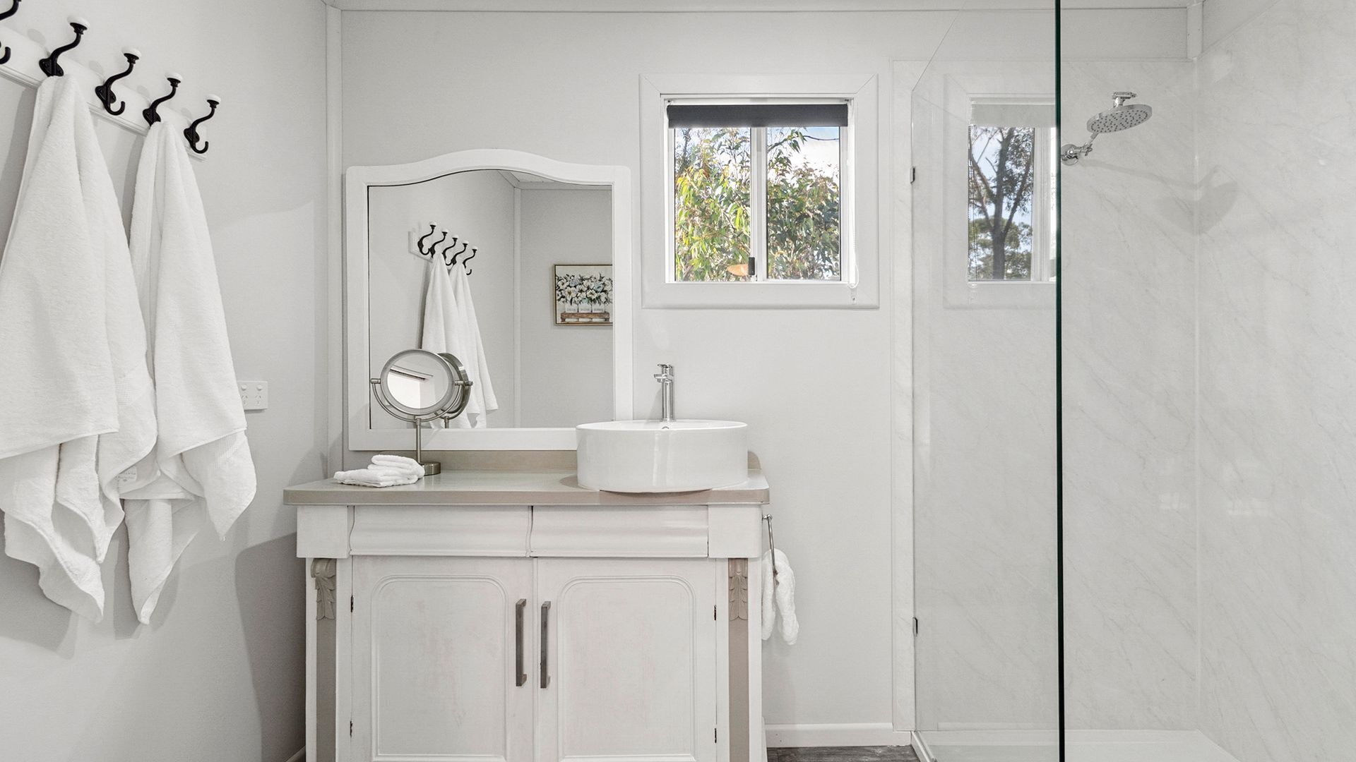 A bathroom with a white vanity, a round mirror, a sink, and a shower.
