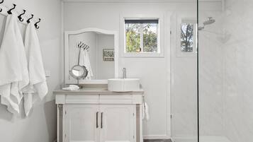 A bathroom with a white vanity, a round mirror, a sink, and a shower.