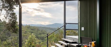 A covered outdoor dining area with a view of a forested landscape and mountains.