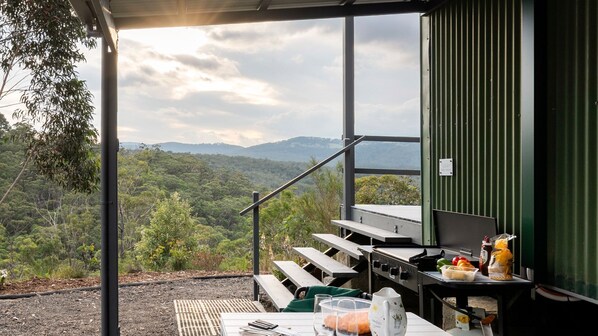 A covered outdoor dining area with a view of a forested landscape and mountains.