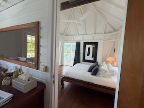 A bedroom with a bed, a bedside table with toiletries, a mirror, and a view of the outdoors.